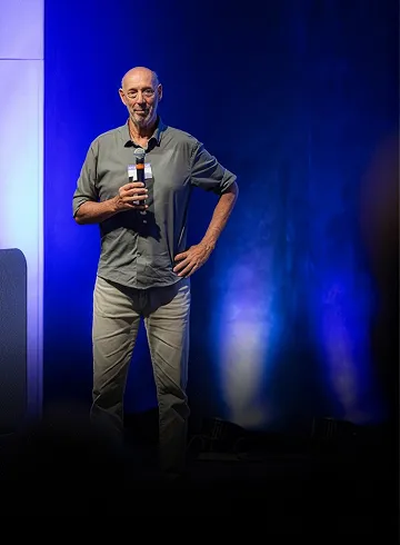 Beto Pandiani de pé no palco, com microfone na mão