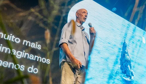 Beto Pandiani palestrando no palco, diante de um telão com o mar